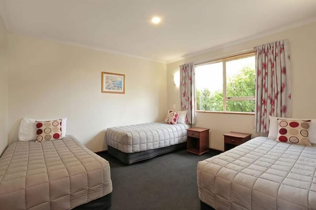 A room with three beds, a window with curtains, a small desk, and a framed picture on the wall.