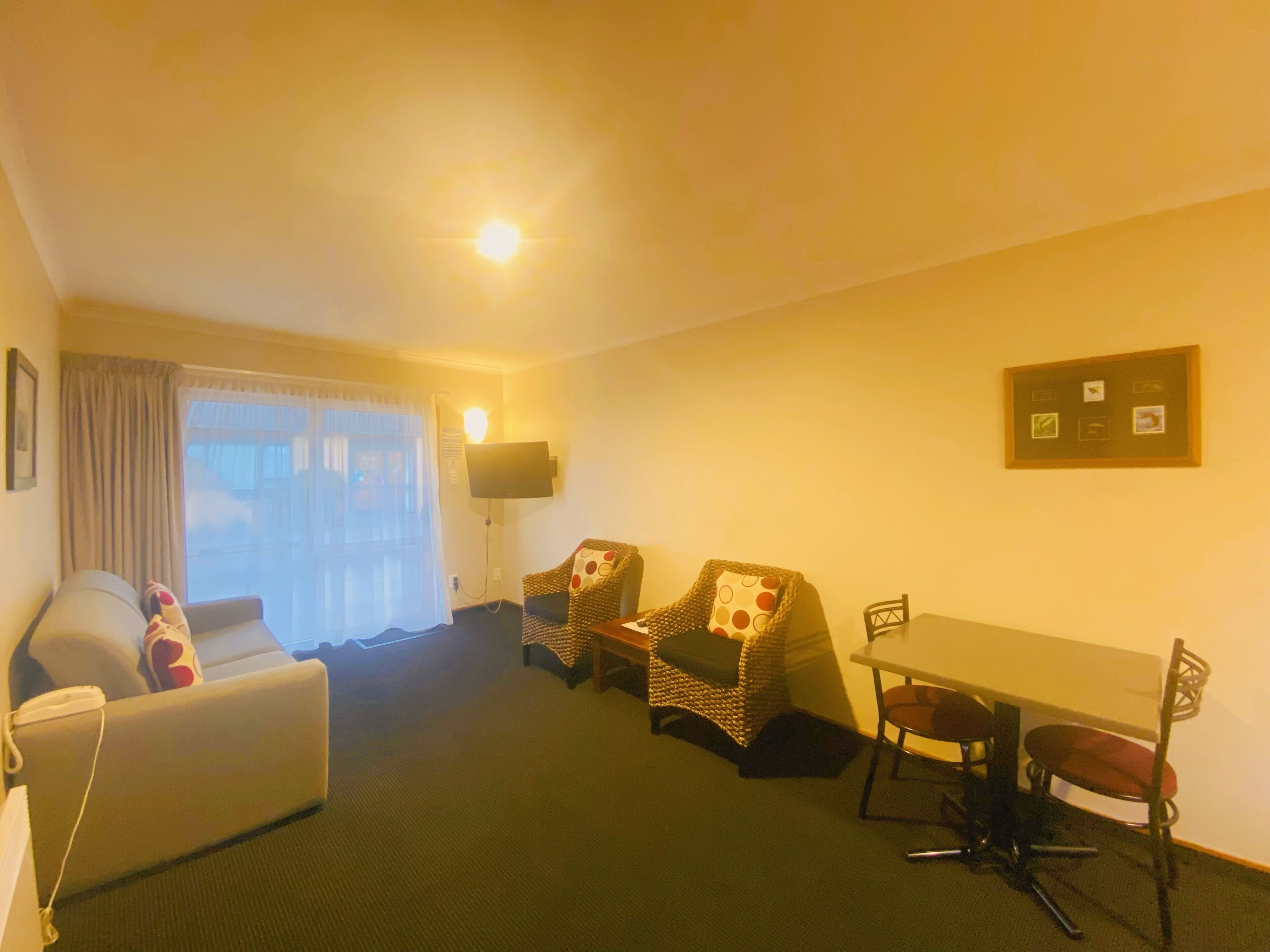 A hotel room with a sofa, two armchairs, a dining table with chairs, a flat-screen TV, and a wall-mounted picture.