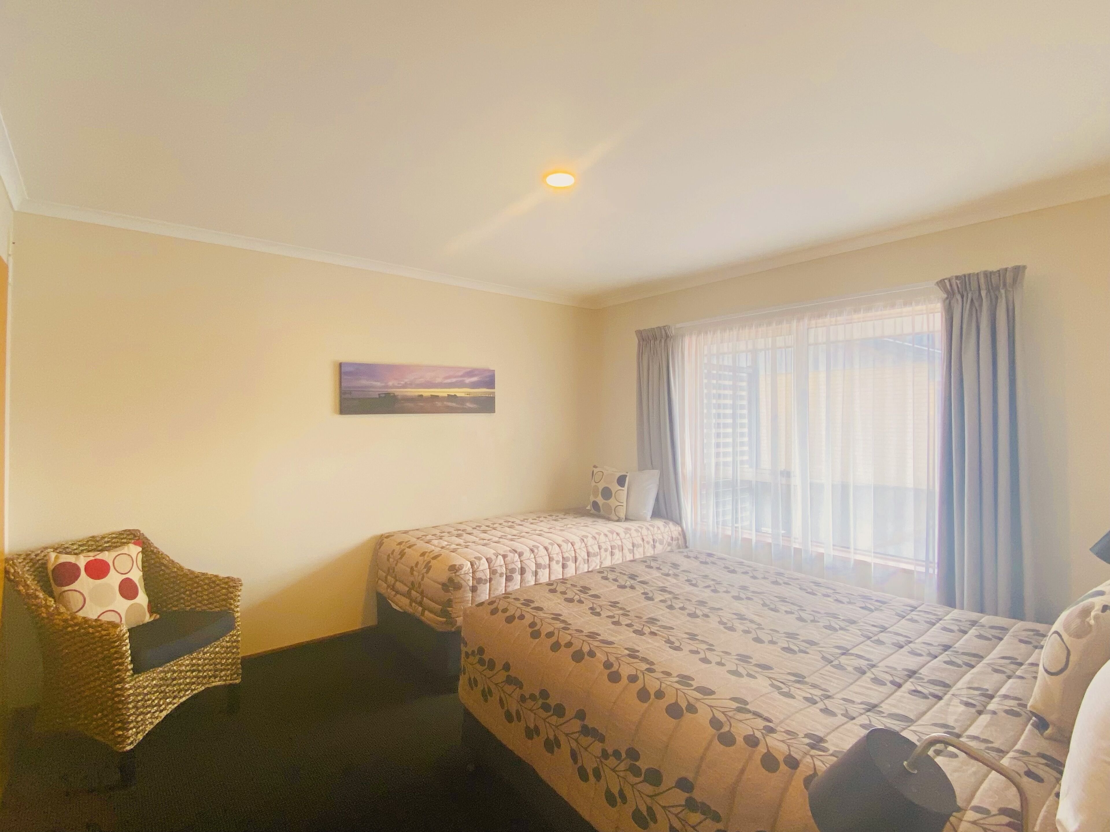 Una habitación con dos camas, una silla, un cuadro en la pared y un ventanal con cortinas.
