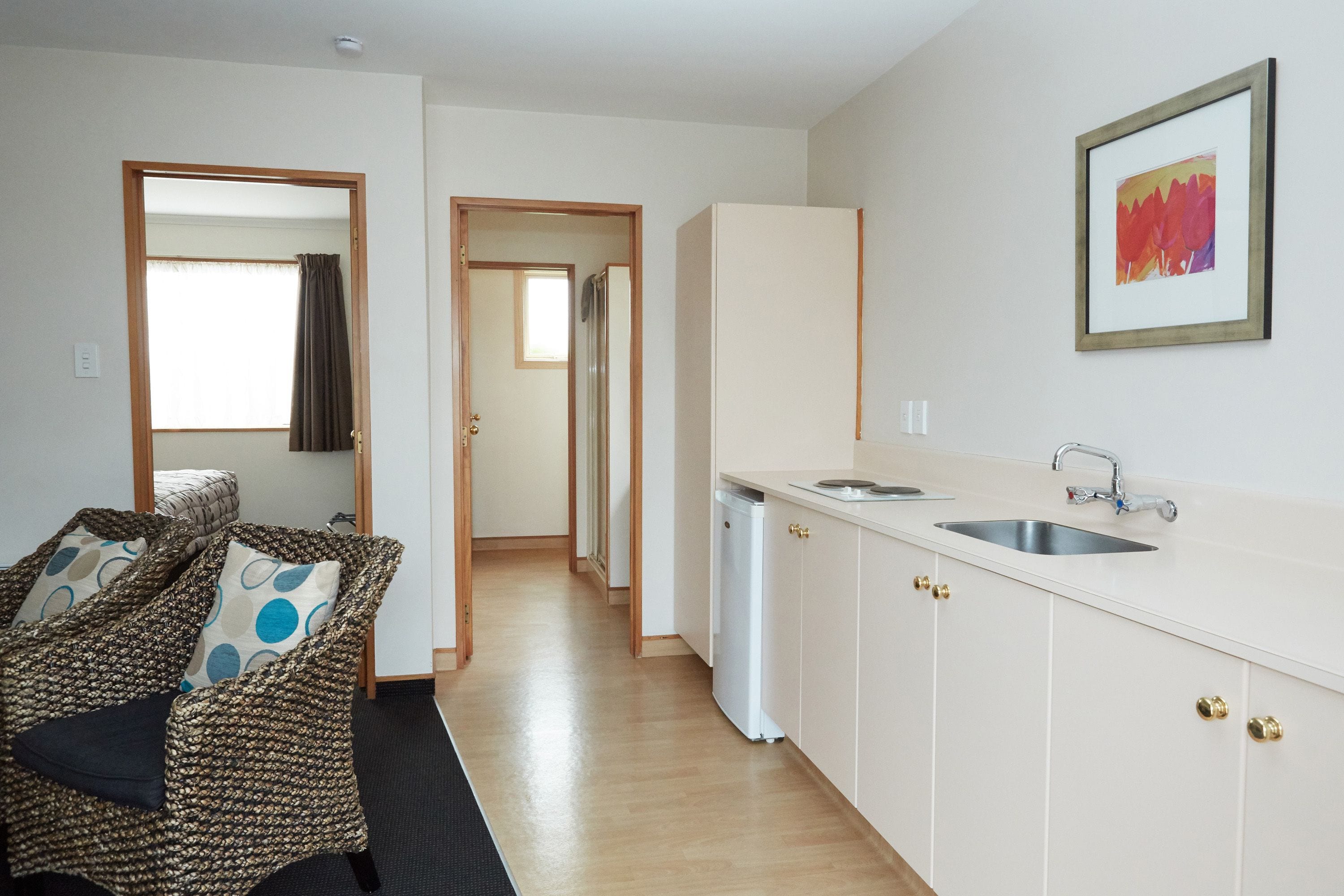 A compact kitchen with a sink and cabinets, a dining area with a patterned chair, and a hallway leading to another room.