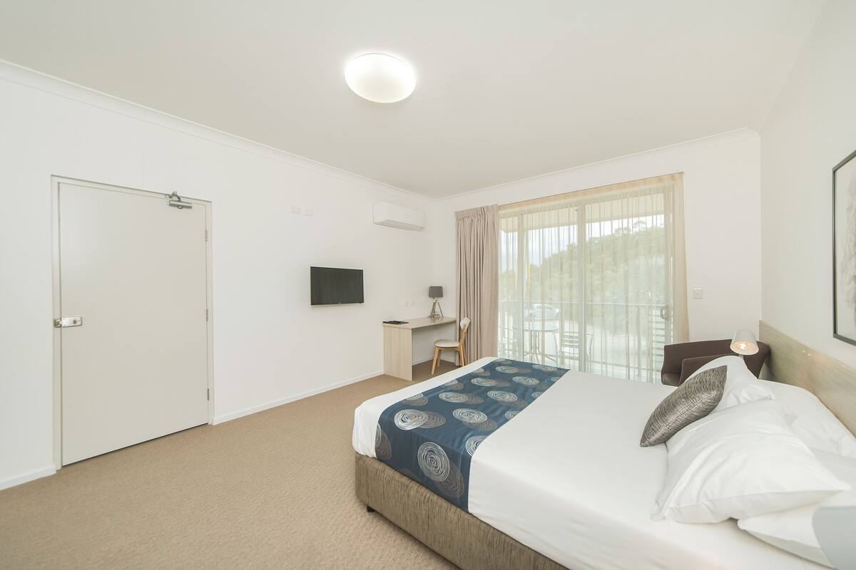 A hotel room with a bed, a desk, a chair, a TV, and a window with curtains.