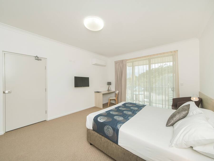 A hotel room with a bed, a desk, a chair, a TV, and a window with curtains.