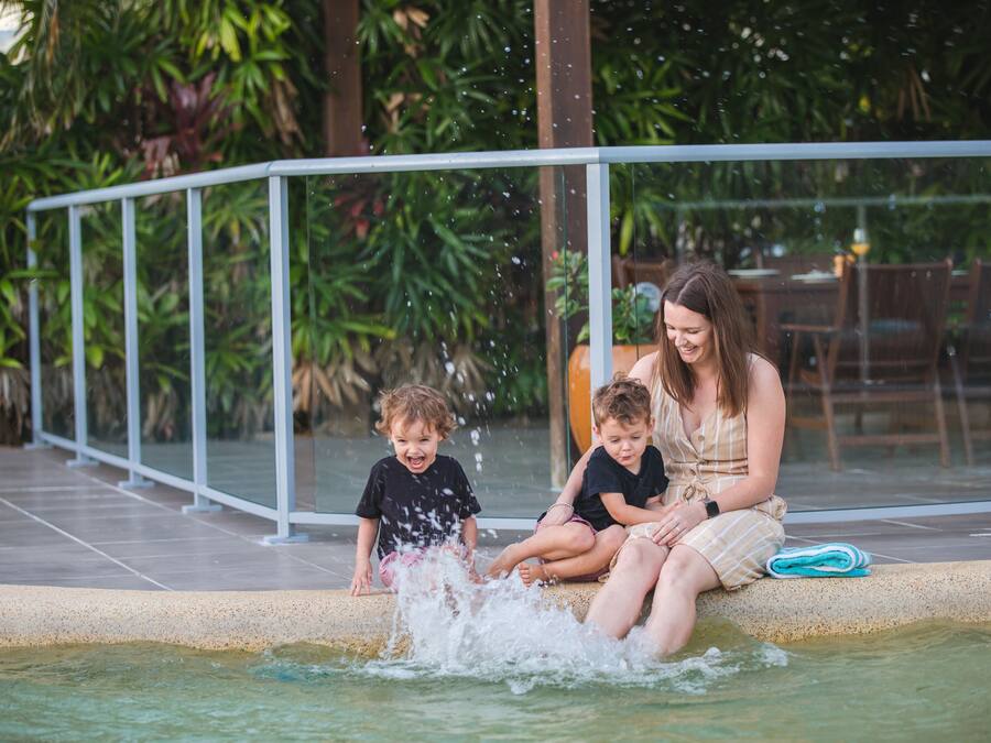 A pool area with a metal railing, water splashing, and greenery in the background.