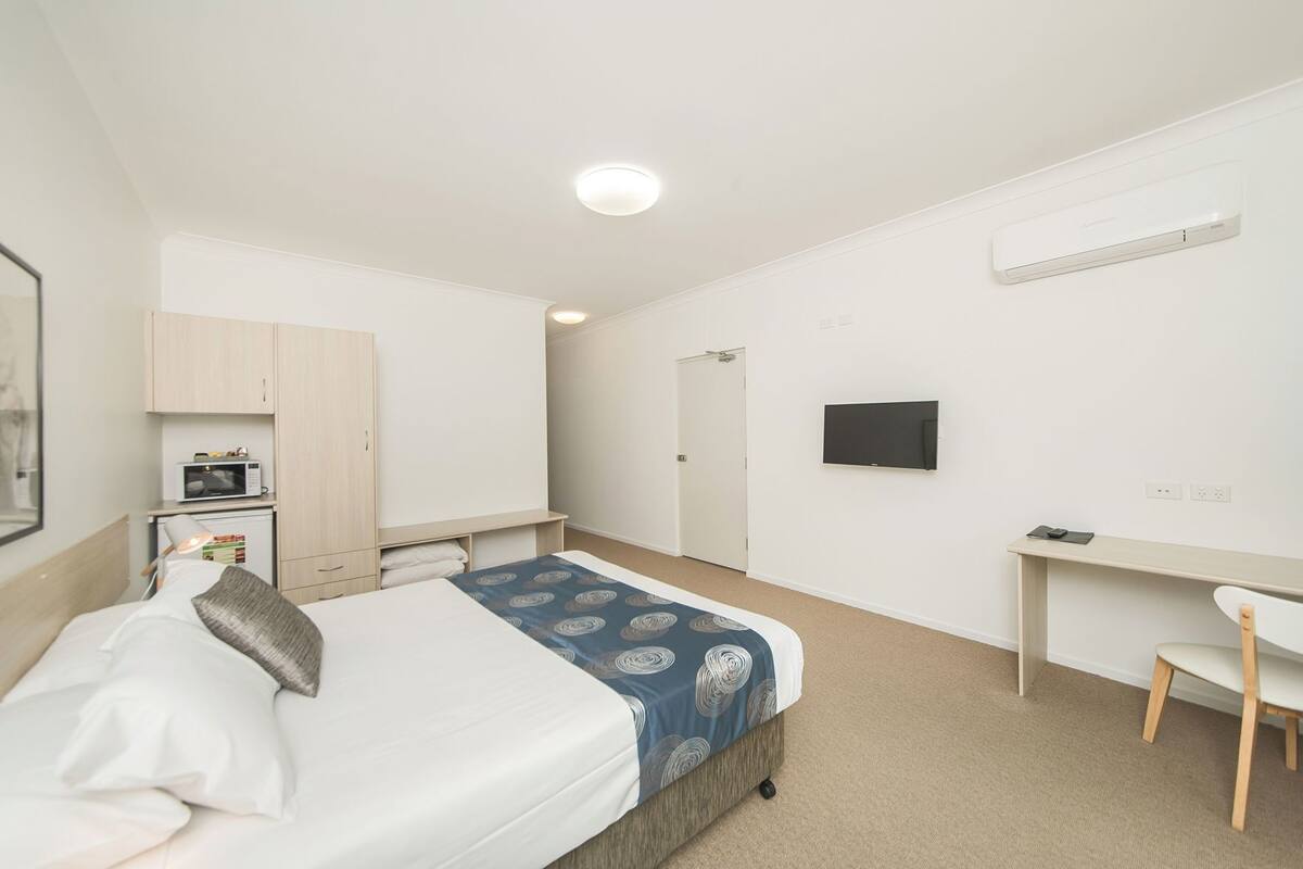 A bedroom with a bed, a desk, a TV, and a microwave.