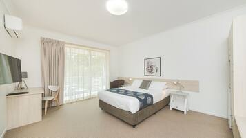 A hotel room with a bed, a desk, a chair, a TV, a bedside table, and a window with curtains.