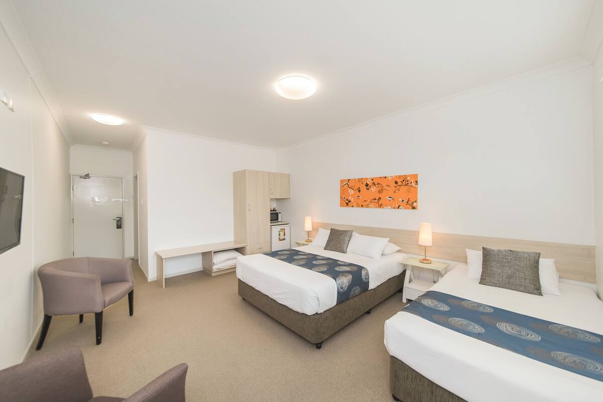A hotel room with a large bed, a smaller bed, a desk, a chair, and a TV.