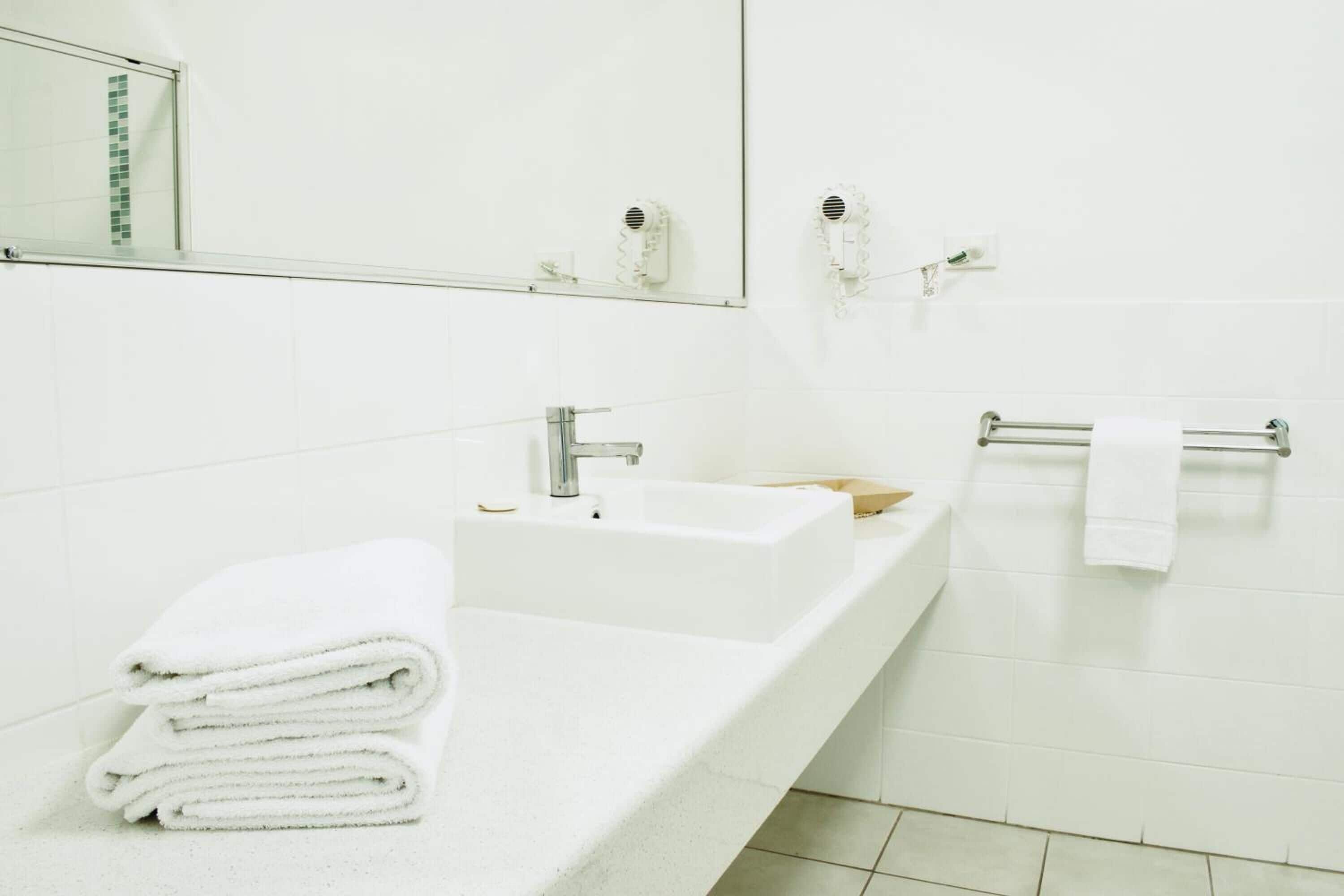 Un baño moderno con un lavamanos blanco, un espejo y un perchero para toallas.