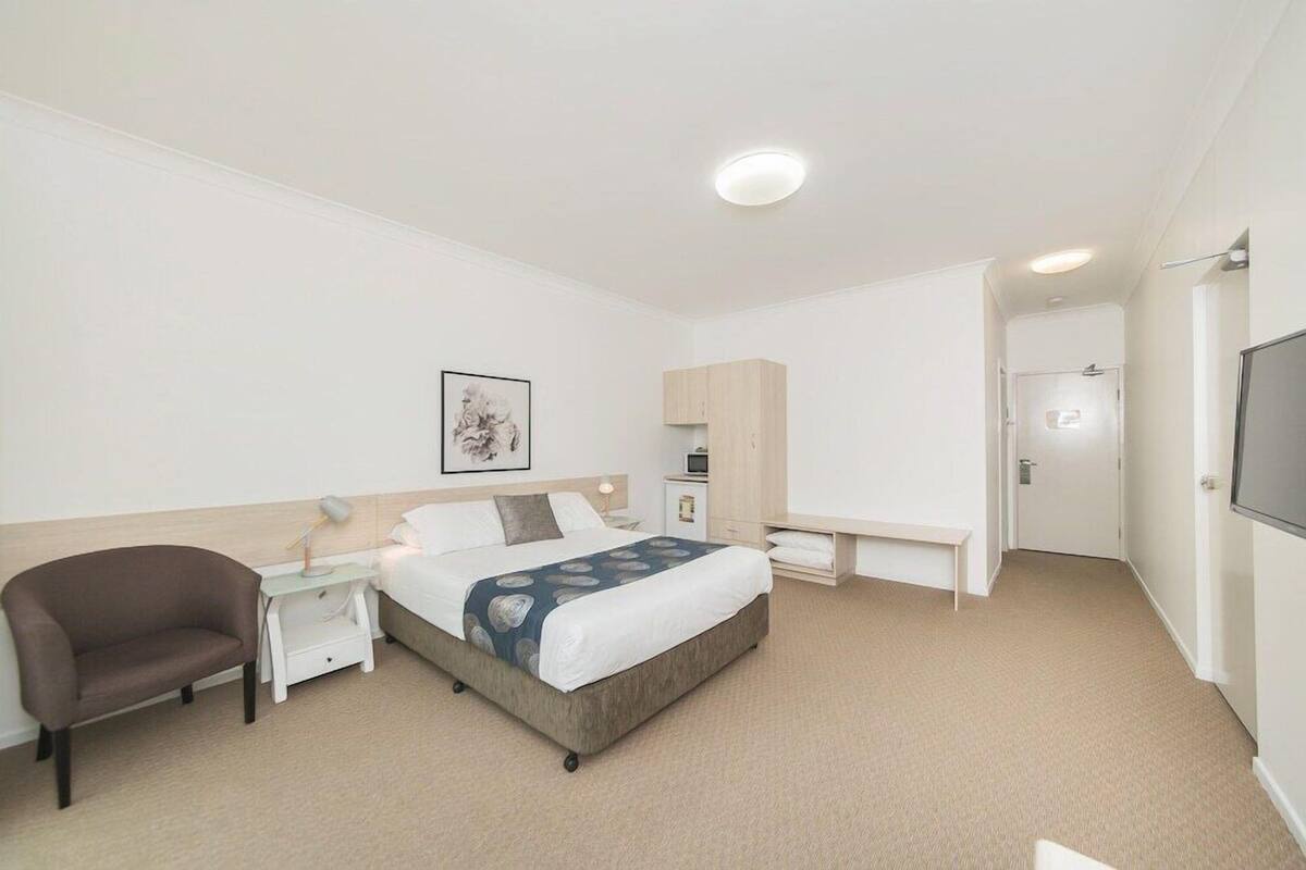 A hotel room with a bed, a chair, a desk, a TV, and a door.