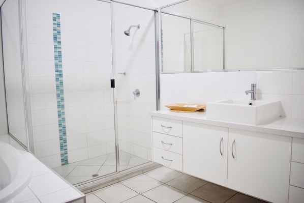 Un baño moderno con ducha envuelta en vidrio, un lavamanos blanco y un espejo sobre él.