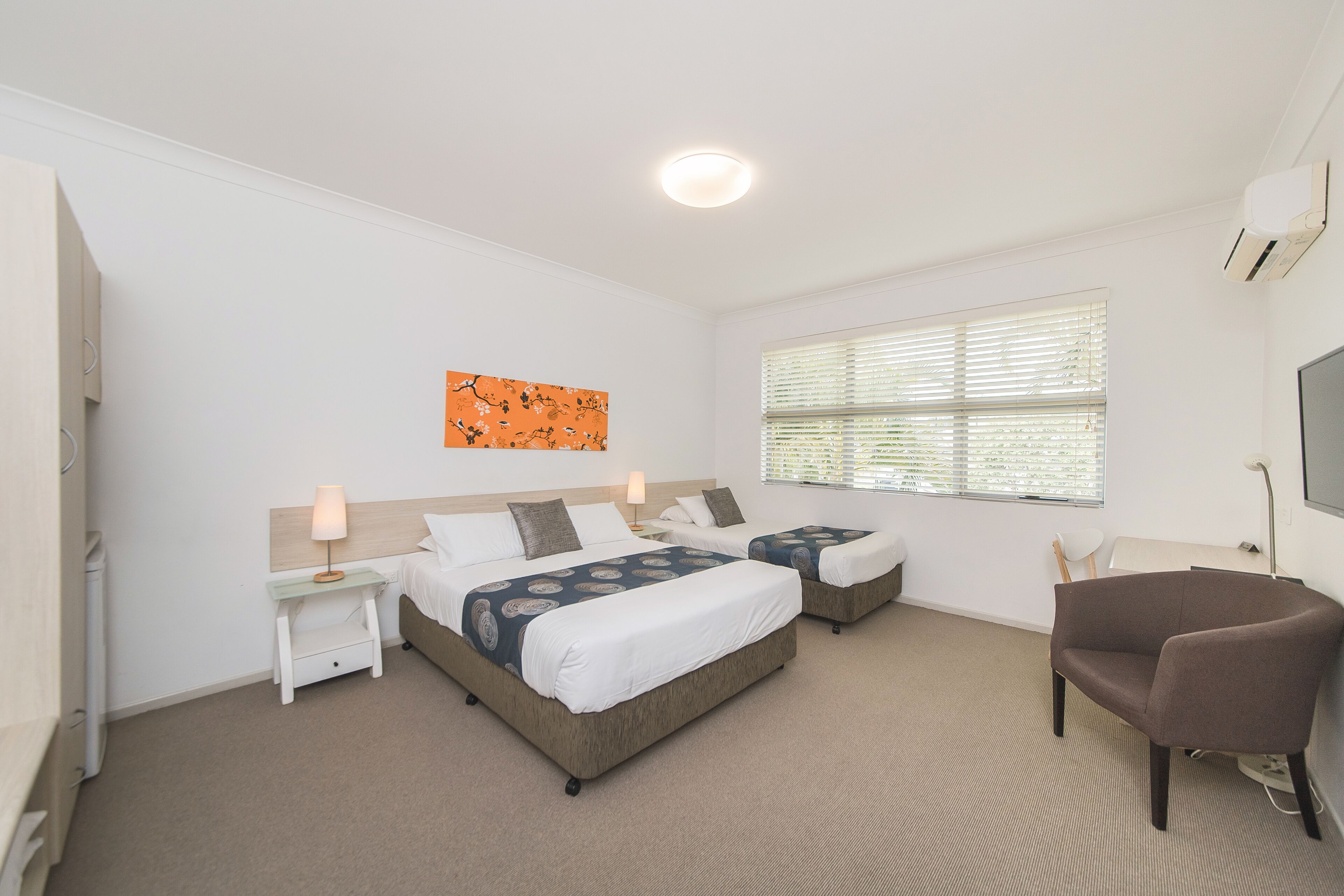 A hotel room with two beds, a desk, a chair, and a window with blinds.