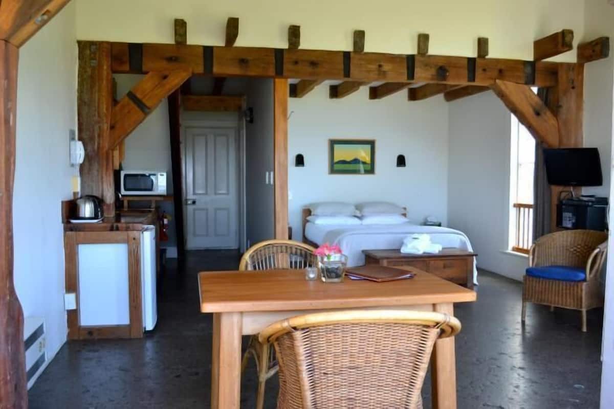 A cozy room with a bed, a dining table, wicker chairs, a small kitchenette, and a television.