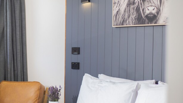 Ein Hotelzimmer mit einem Bett, einem Sessel, einem Wandbild und einem kleinen Tisch mit einer Vase.