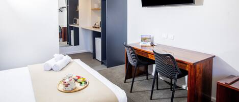 Habitación de hotel con cama, escritorio con silla, televisor de pantalla plana montado en la pared y una pequeña zona de kitchenette.
