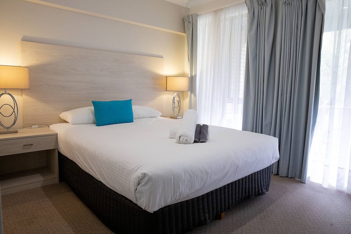 Een hotelkamer met een groot bed, twee nachtkastjes, een lamp en een raam met gordijnen.