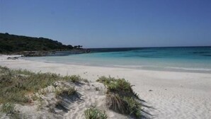 Una playa con agua turquesa cristalina, arena blanca y vegetación escasa.