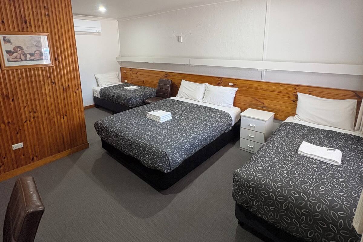 A hotel room with two beds, a wooden panel wall, a framed picture, and a white ceiling light.
