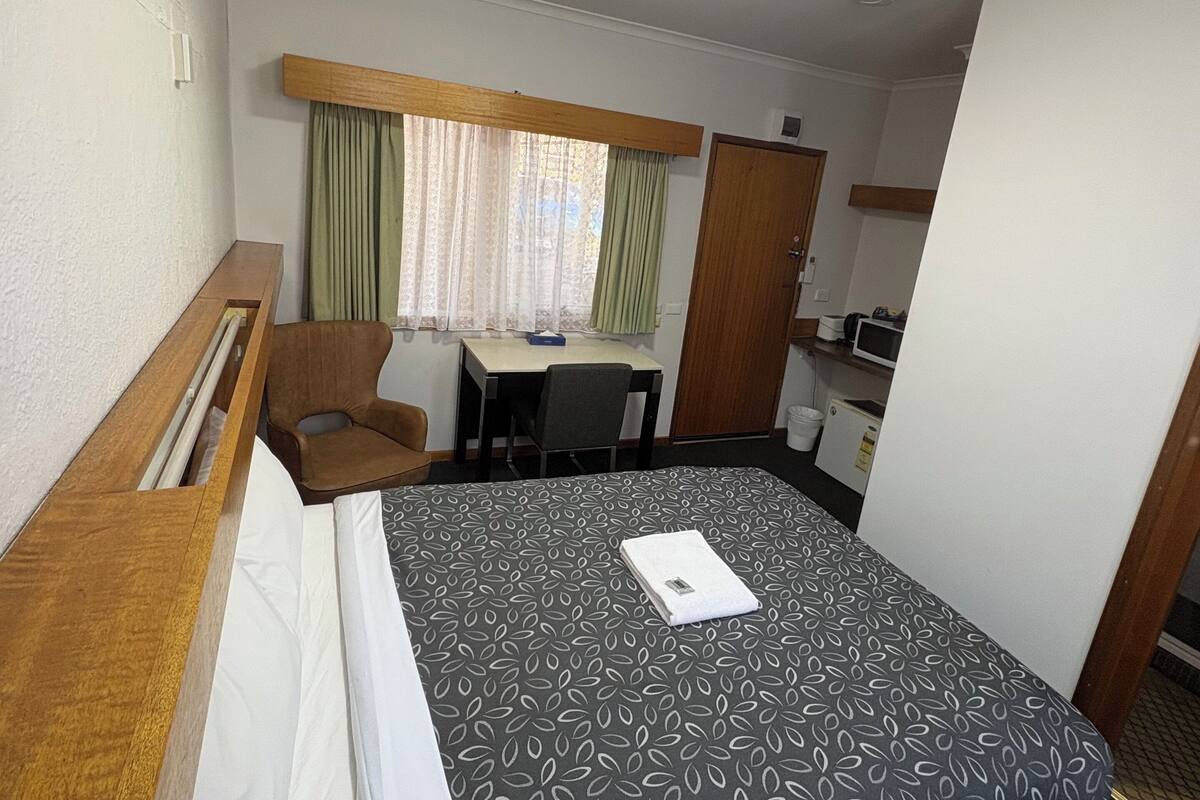 A hotel room with a bed, a desk, a chair, and a window with curtains.
