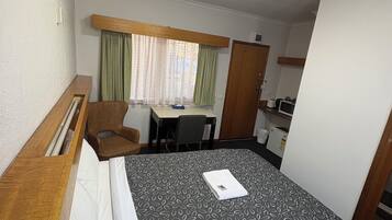 Une chambre d’hôtel avec un lit, un bureau, une chaise et une fenêtre avec des rideaux.