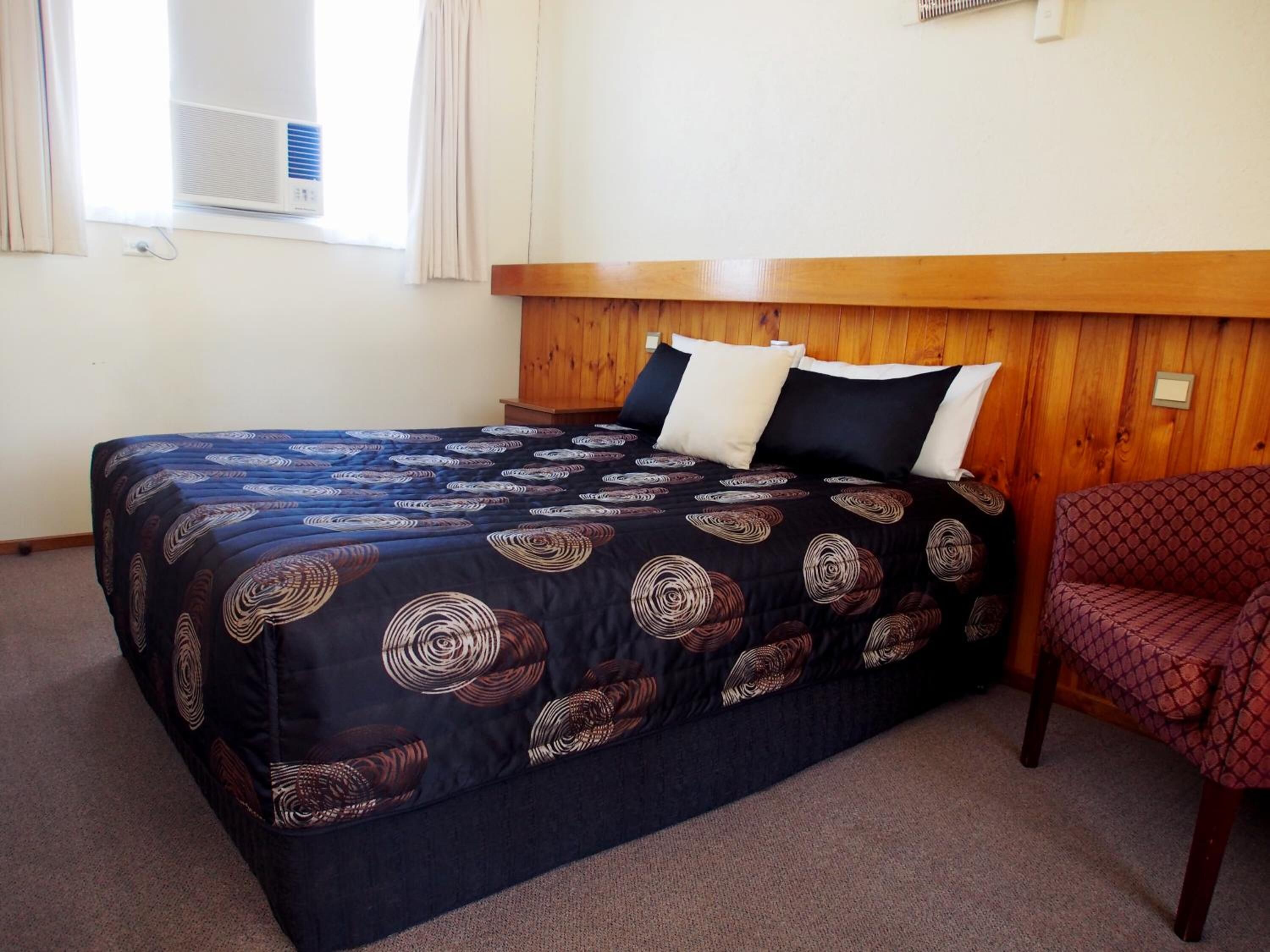 A hotel room with a bed, wooden headboard, and a single chair.