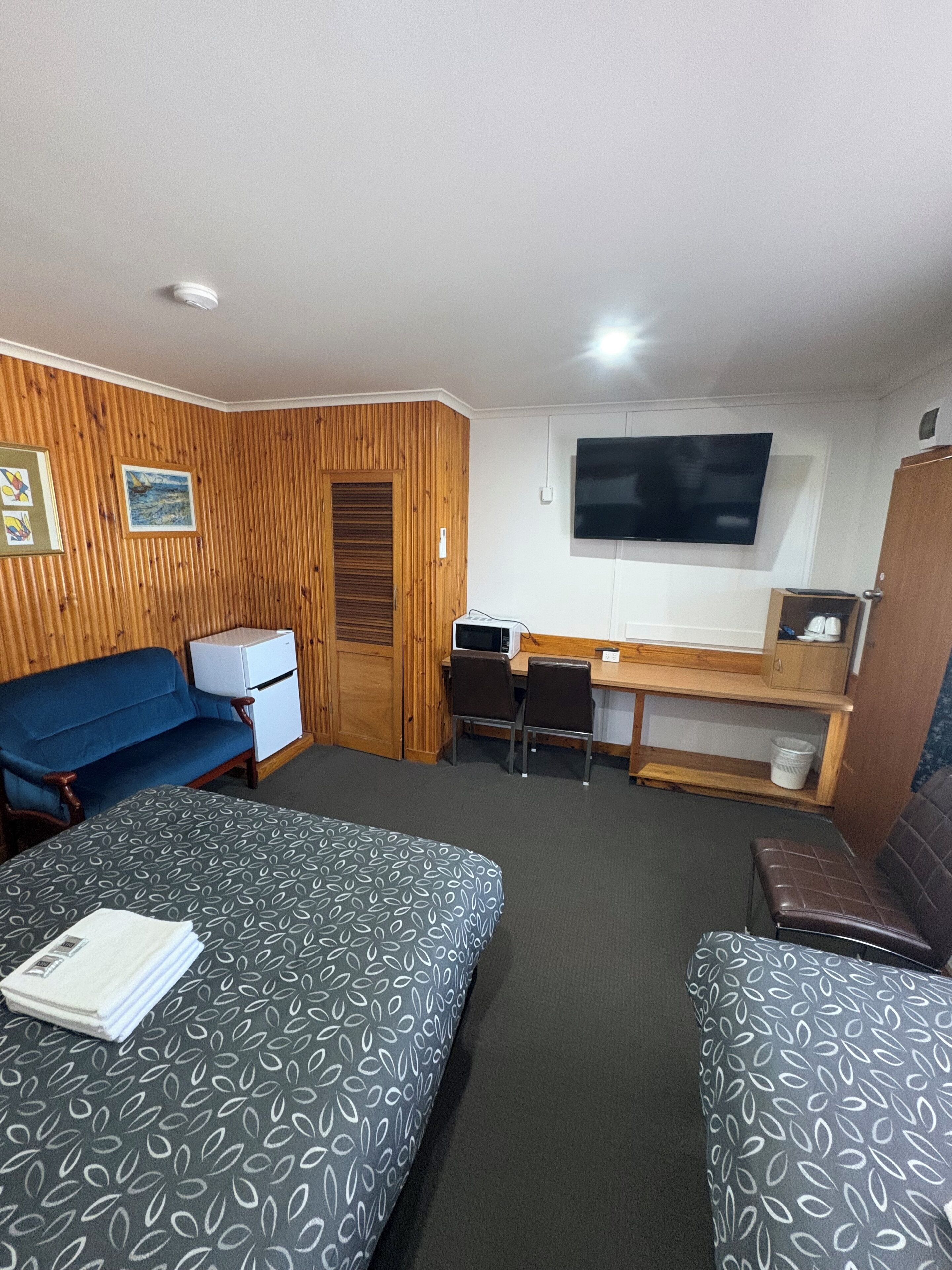 A compact room with two beds, a desk, a television, and a kitchenette.