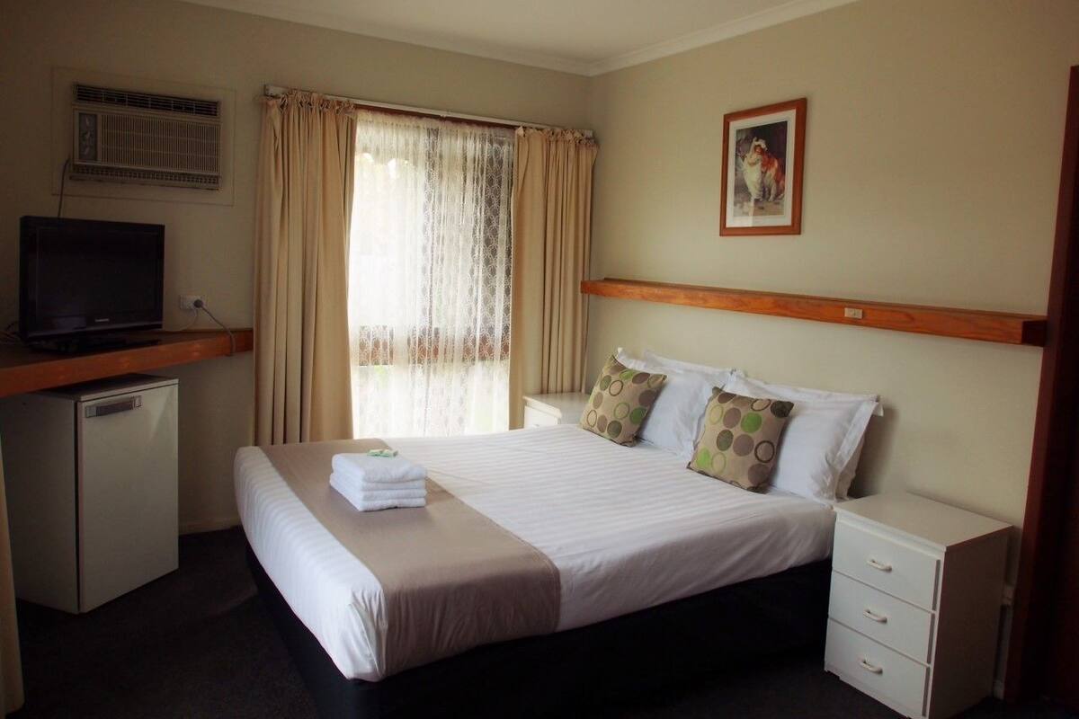 A hotel room with a bed, a desk with a television, a small refrigerator, and a window with curtains.