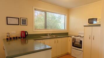 A kitchen with a window, sink, stove, and cabinets.