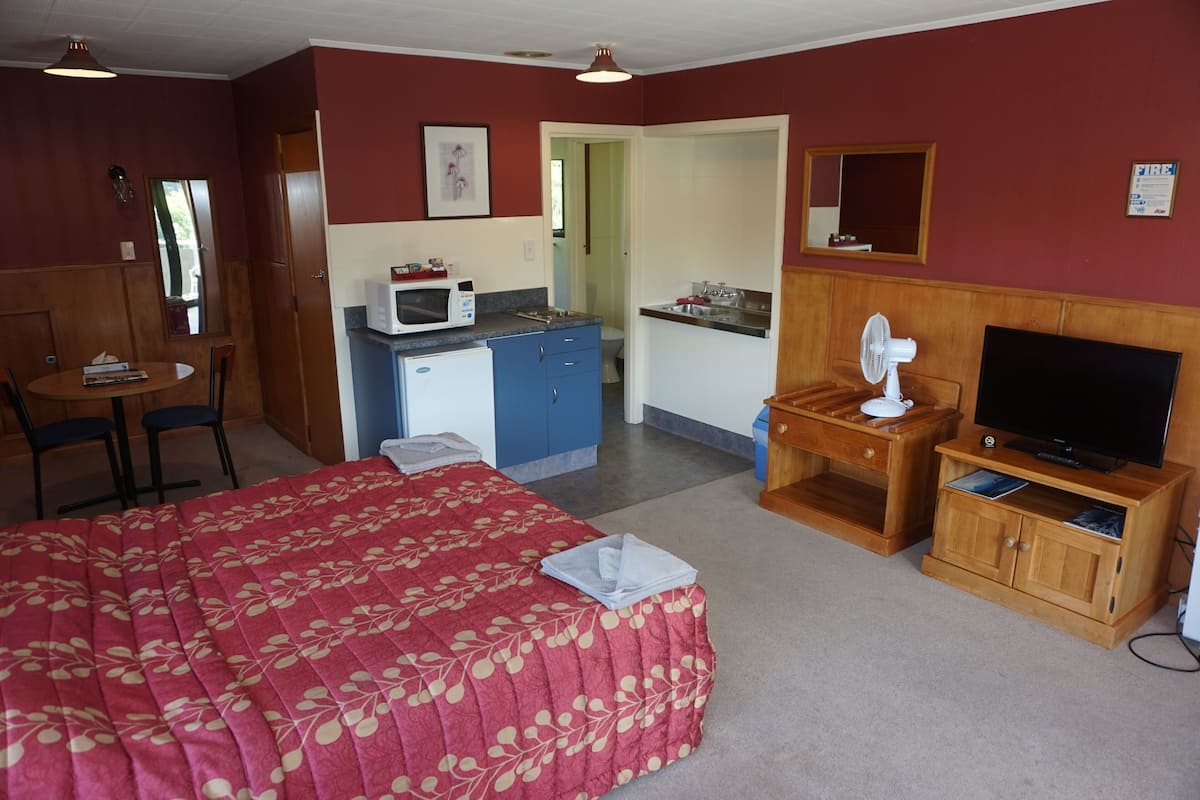 A room with a bed, a desk, a microwave, a television, and a small kitchenette.