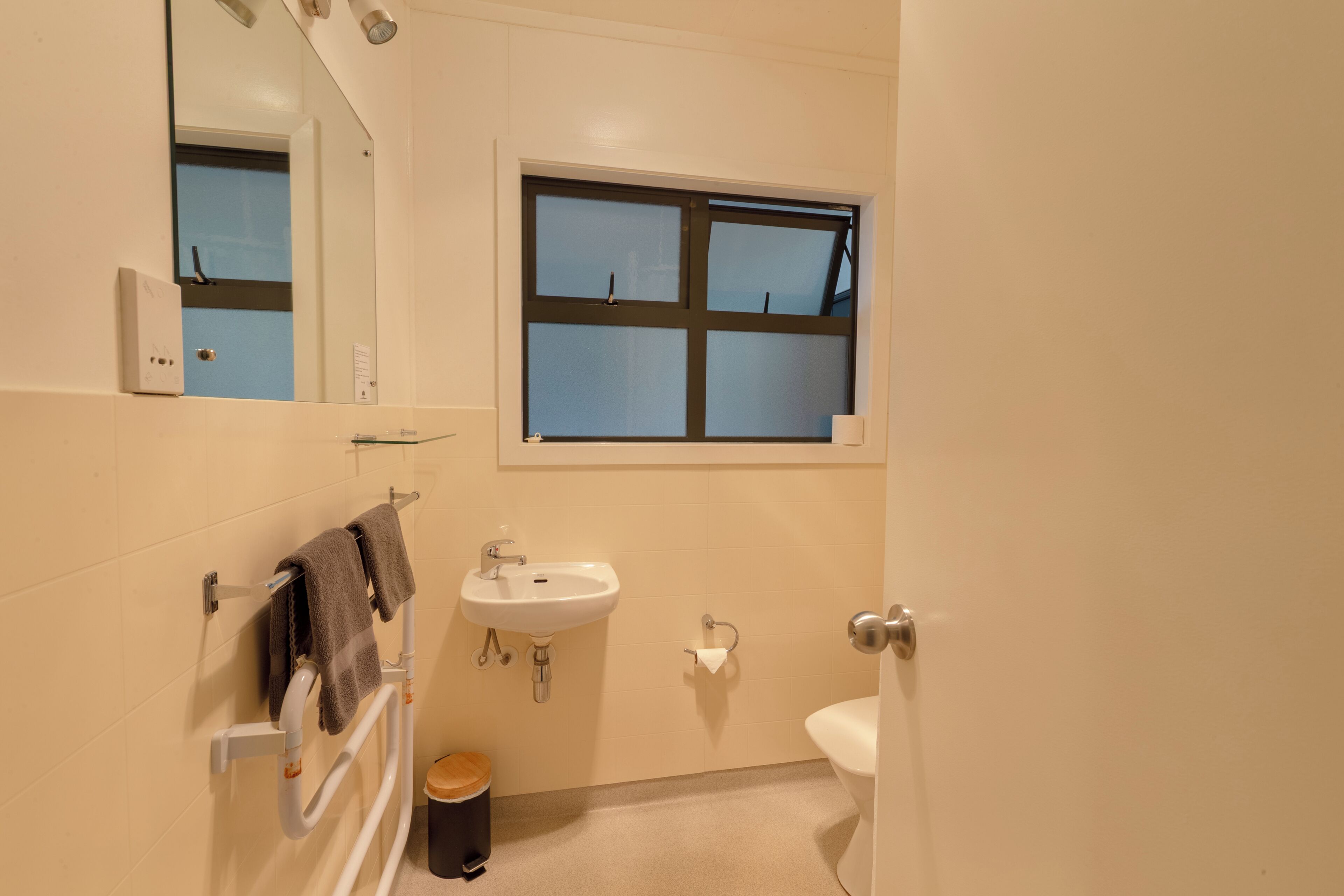 Un baño con lavabo, espejo, ventana y toallero.