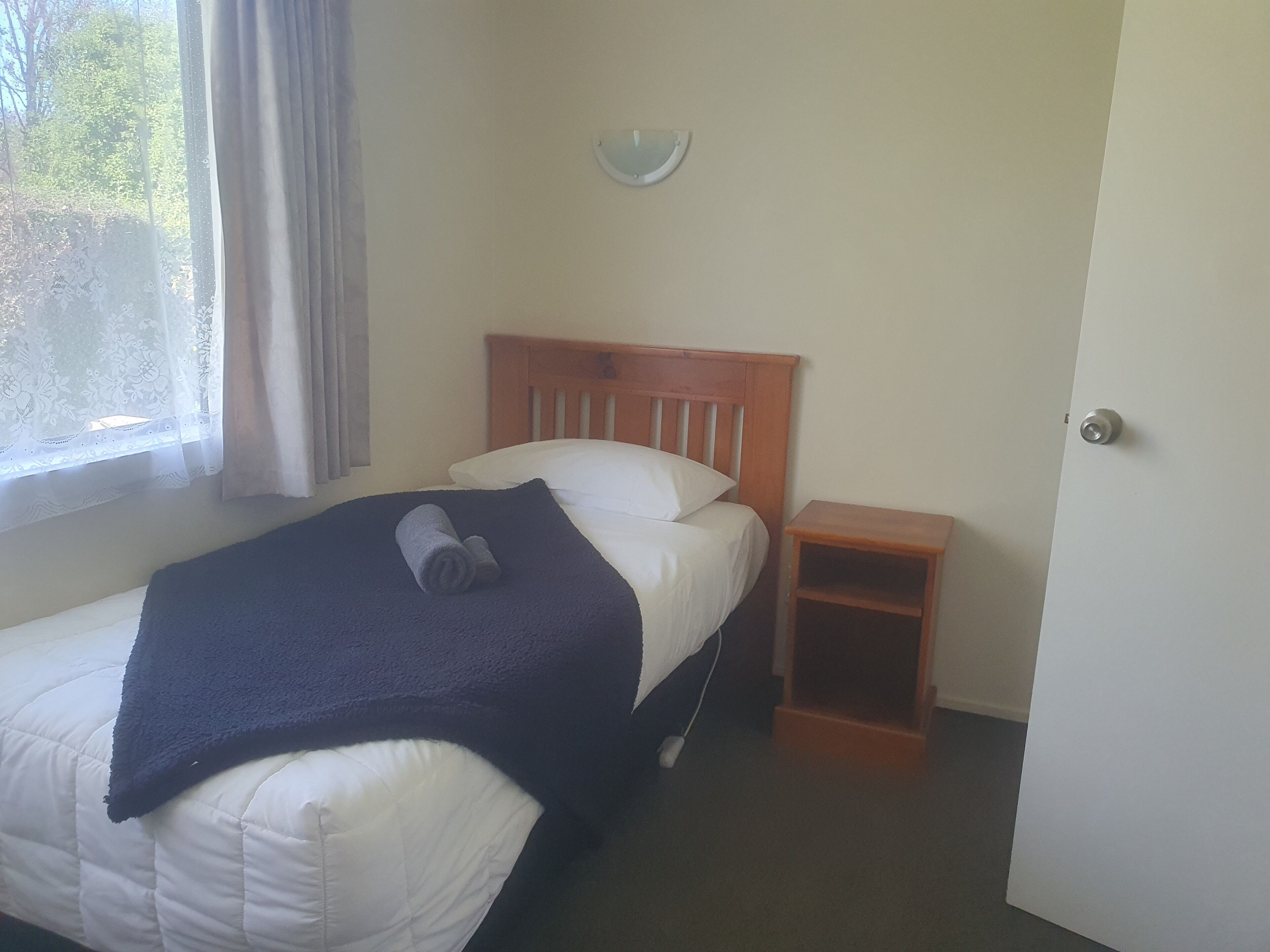 Una cama individual con cabecera de madera, una mesita de noche y una ventana con cortinas.