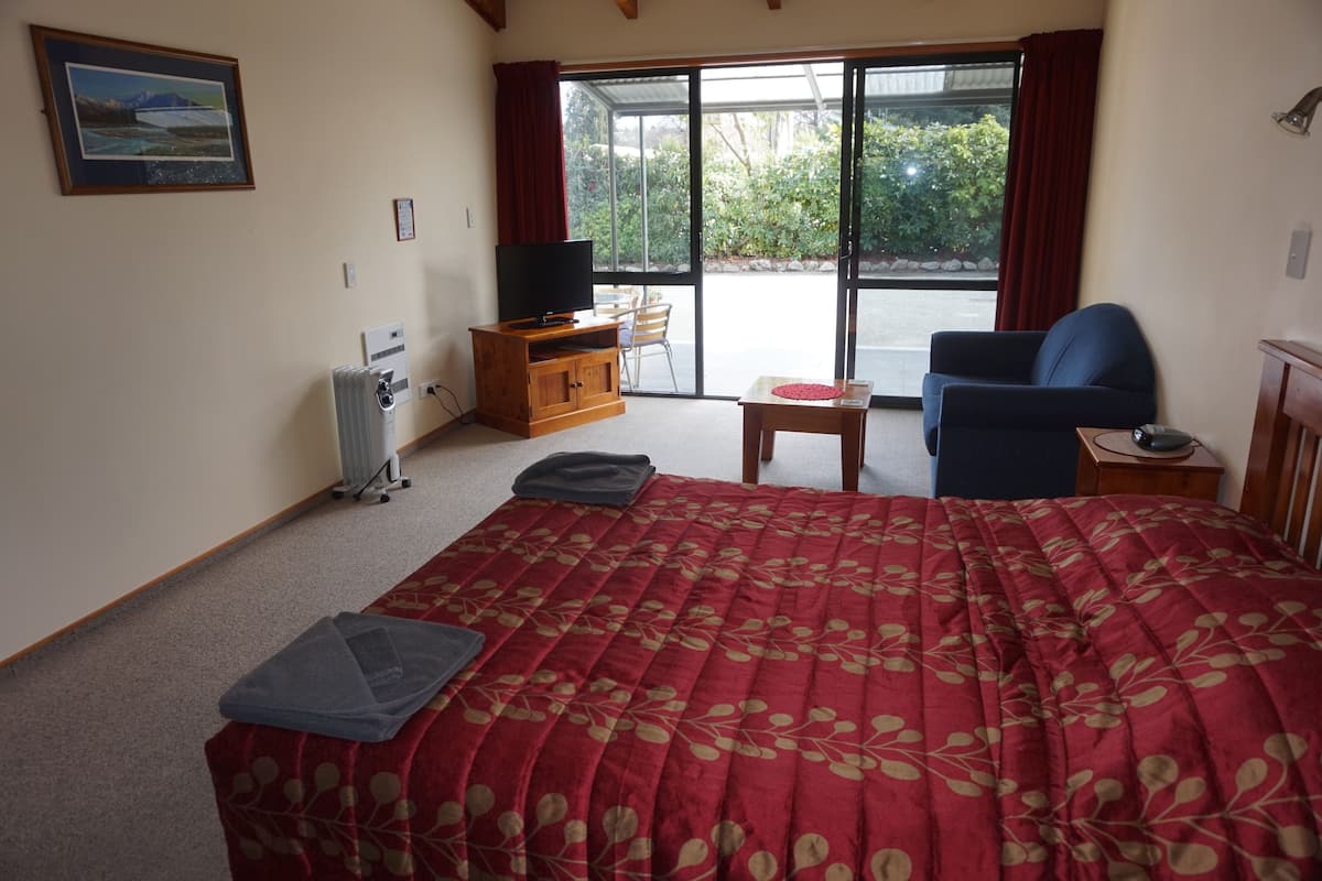 A hotel room with a bed, a TV, a desk, a chair, and a view of the outdoors.