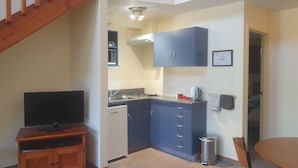 A compact kitchen with a built-in dishwasher, a small sink, and a microwave. There is a wooden entertainment unit with a flat-screen TV. A staircase leads to an upper level.