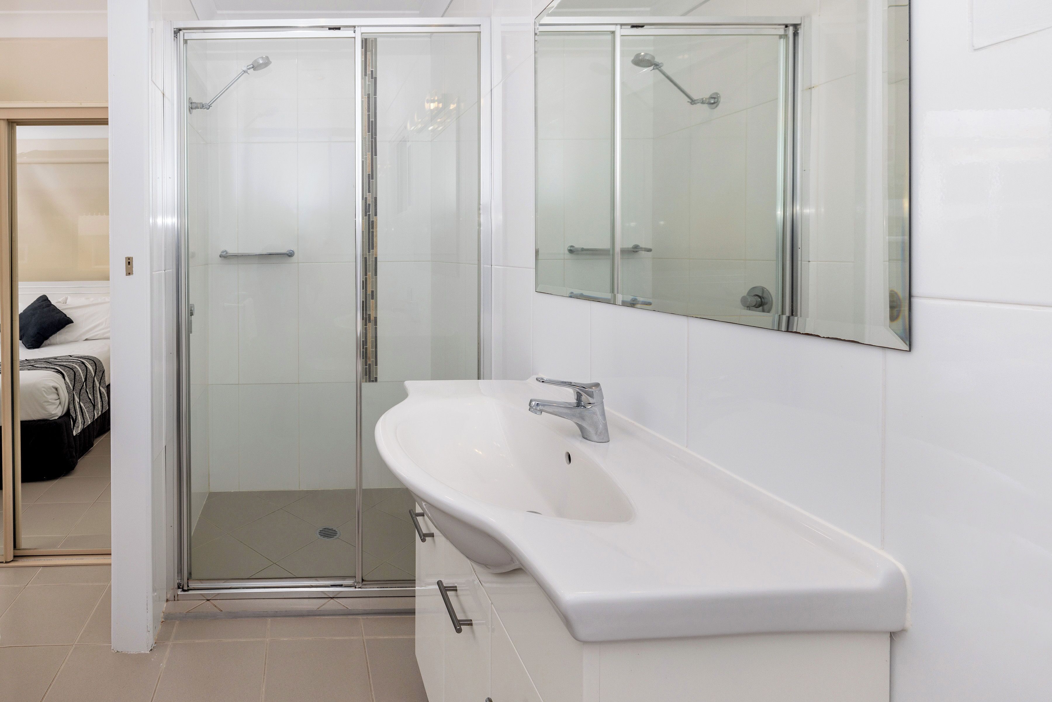 Un baño moderno con ducha de vidrio, lavamanos blanco y un espejo grande.