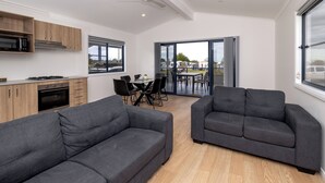 Una sala de estar moderna con dos sofás grises, un comedor con mesa y sillas, y una cocina con armarios de madera y electrodomésticos.