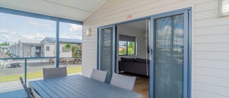 A covered outdoor area with a table and chairs, a sliding glass door leading to an interior space, and a view of other buildings in the background.