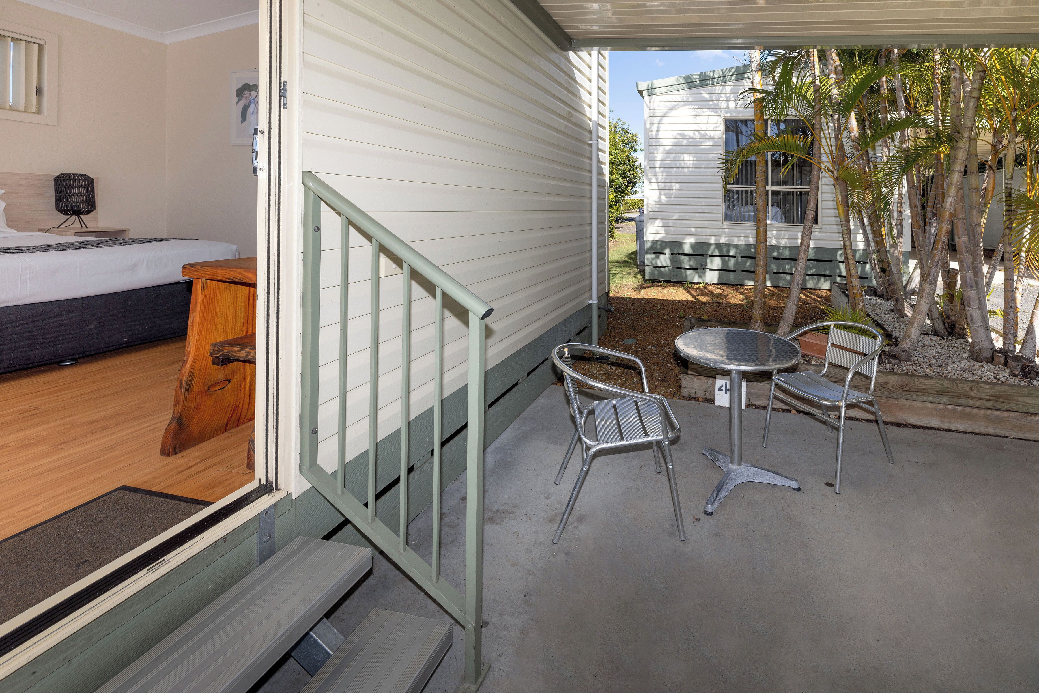 A room with a bed, a small wooden table, and a balcony with chairs and a table.