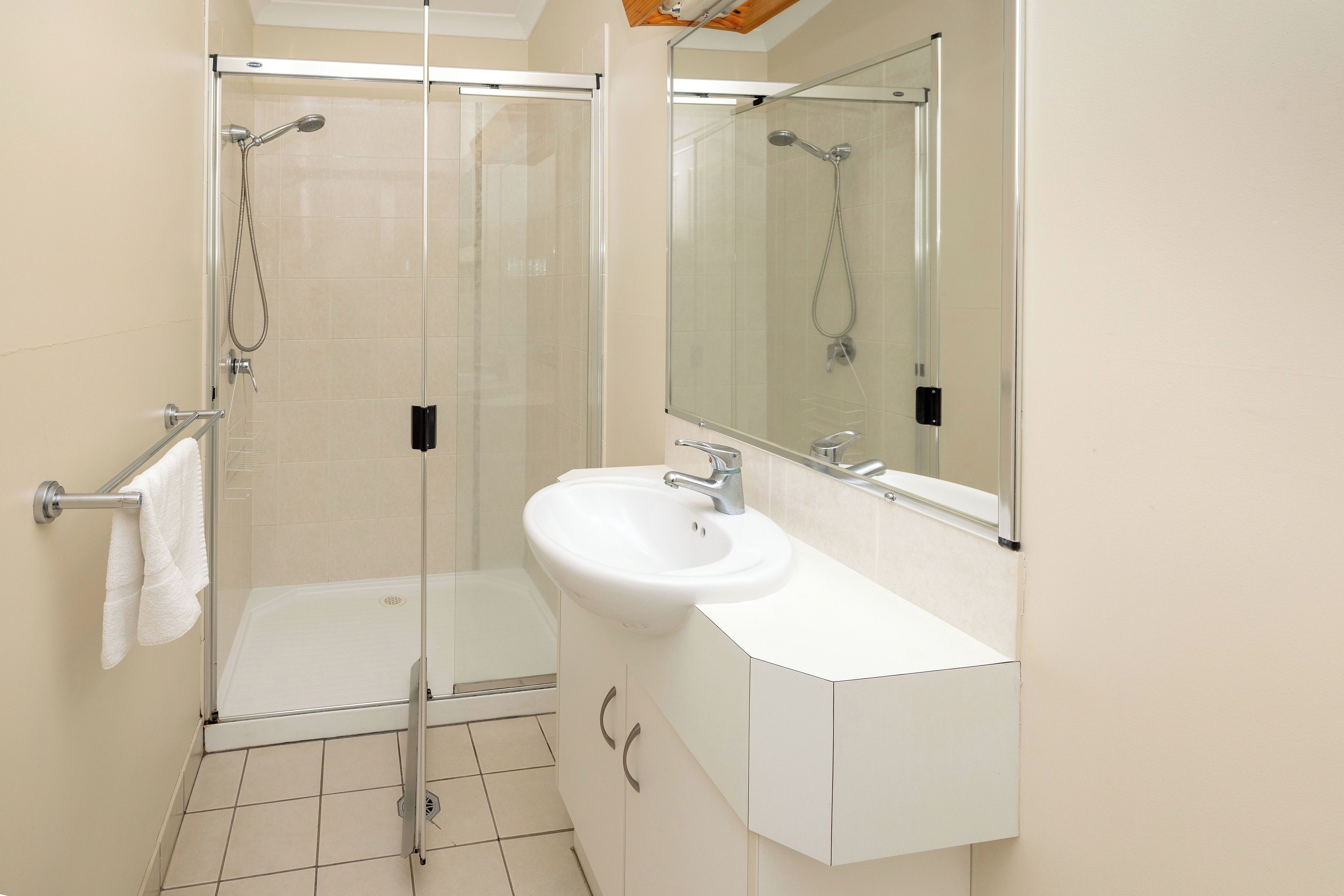Un bagno moderno con doccia vetro, lavandino bianco e uno specchio grande.