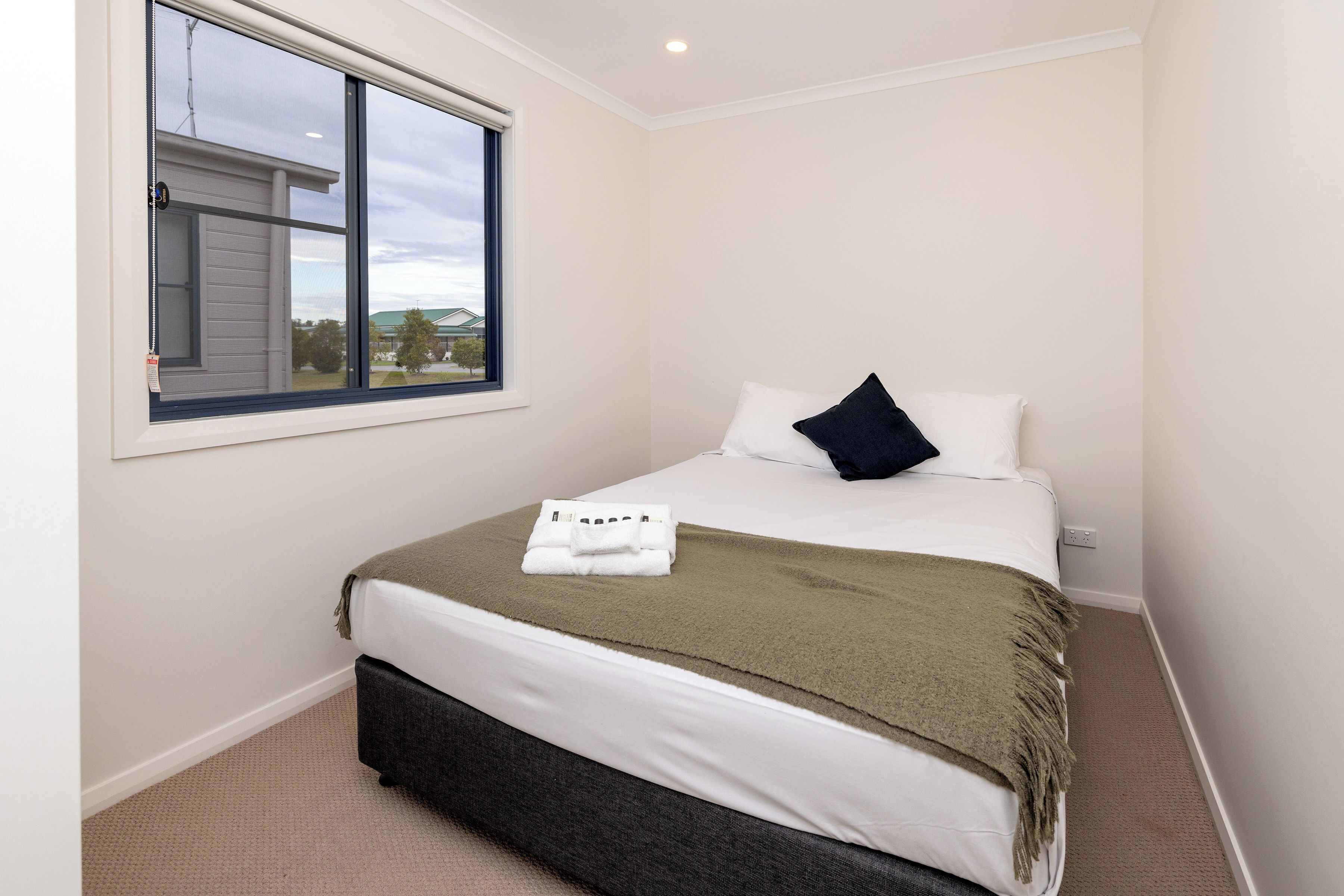 A neatly made bed with a white and green blanket, a dark pillow, and a folded towel on the bed.