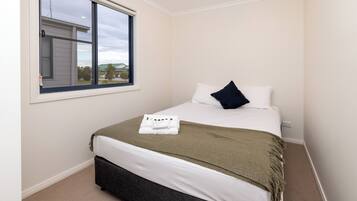 A neatly made bed with a white and green blanket, a dark pillow, and a folded towel on the bed.