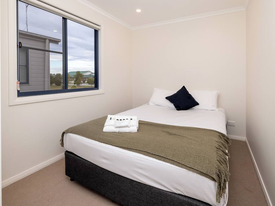 A neatly made bed with a white and green blanket, a dark pillow, and a folded towel on the bed.