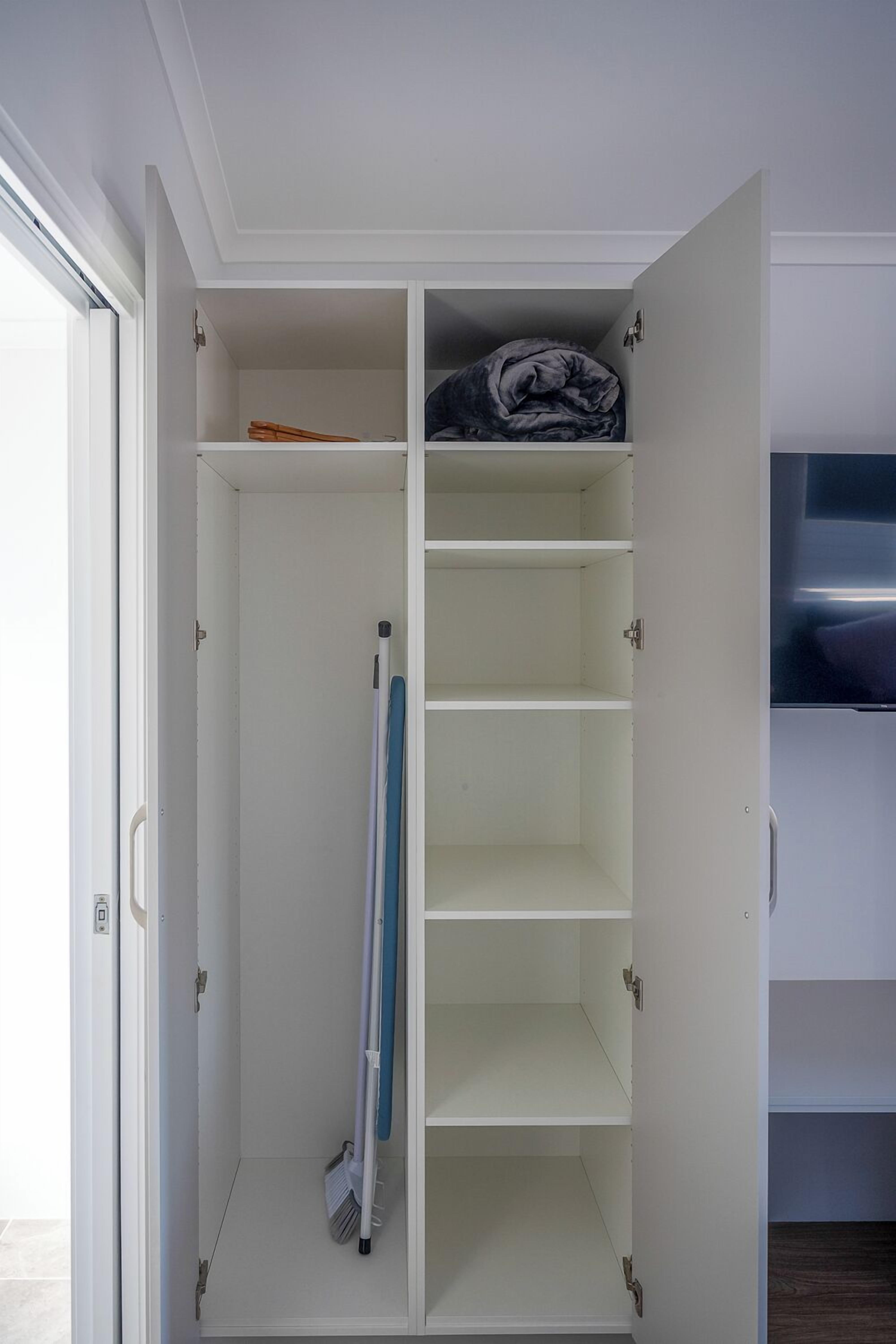 A white wardrobe with multiple shelves and hanging space, a door with a handle, and a small window.