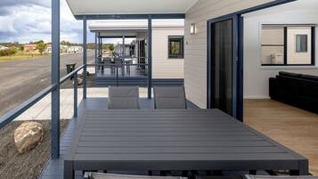 Et overdækket udendørs siddeområde med et bord og stole, en sort sofa, samt udsigt til gaden og husene i baggrunden.