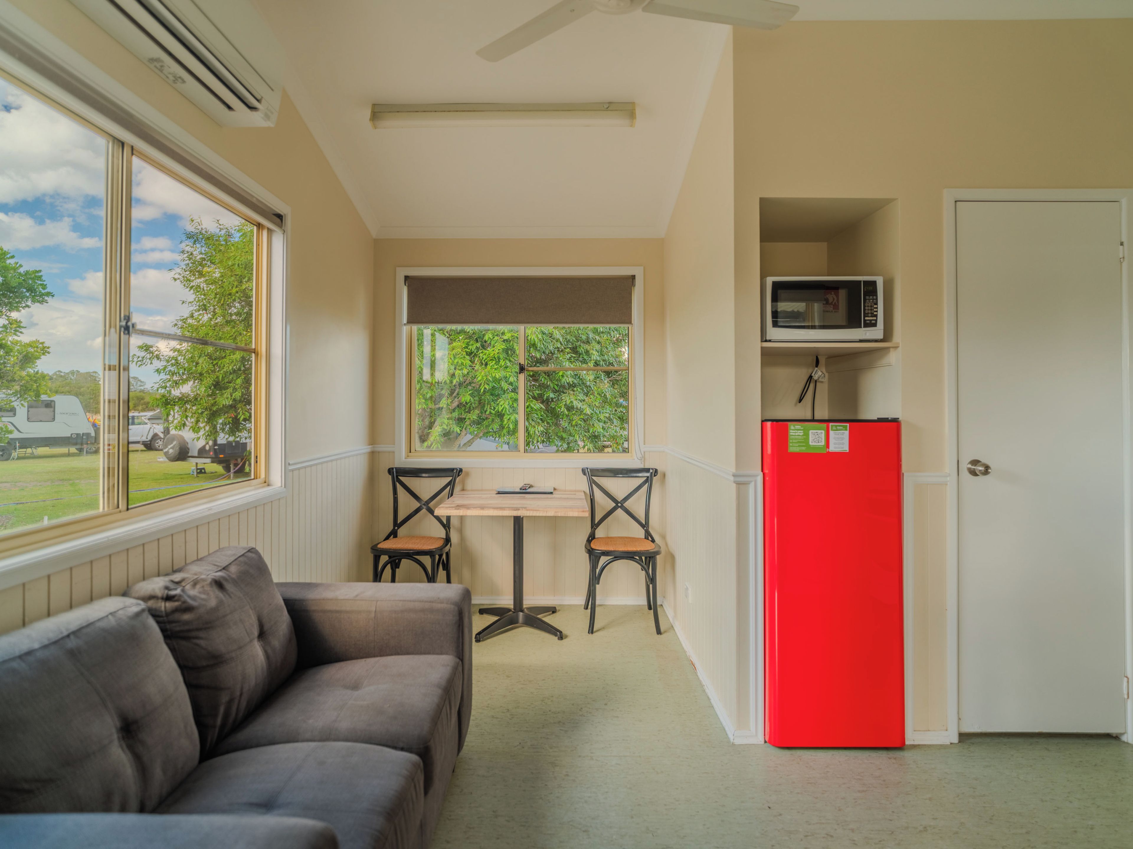 A compact room with a sofa, a dining table with two chairs, a red refrigerator, and a microwave above it.