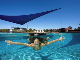 A swimming pool with clear blue water, a person swimming, and a building in the background.