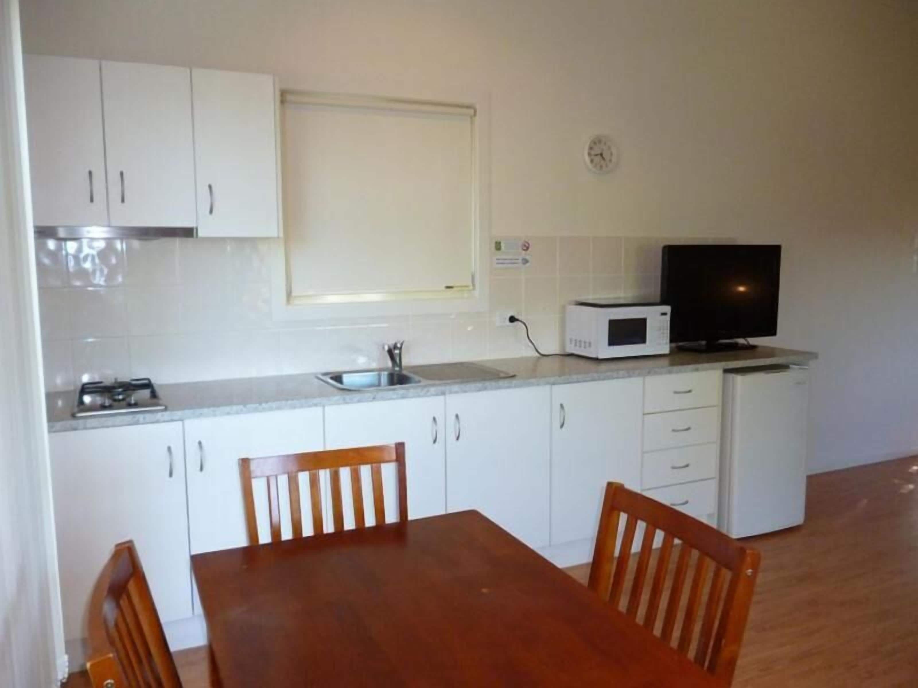 Una cocina compacta con gabinetes blancos, microondas, estufa y televisor.