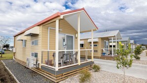 Una casa móvil de un solo nivel con porche cubierto, una pequeña terraza y una unidad de aire acondicionado visible.
