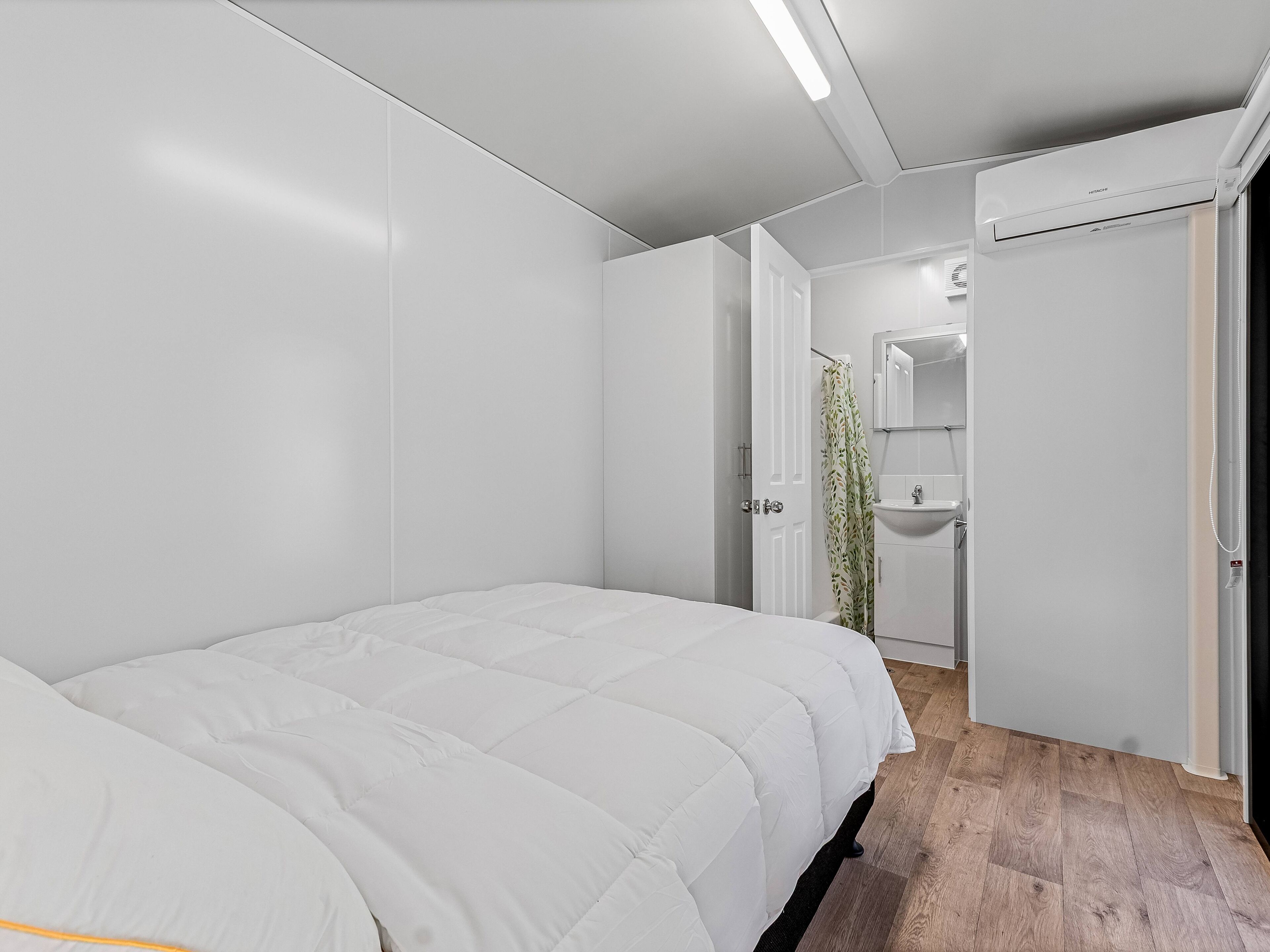 A modern bedroom with a bed, a bathroom with a sink, and a shower.