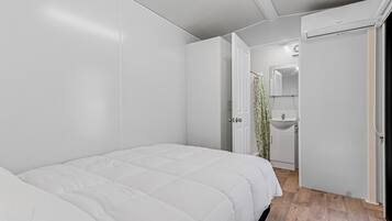 A modern bedroom with a bed, a bathroom with a sink, and a shower.