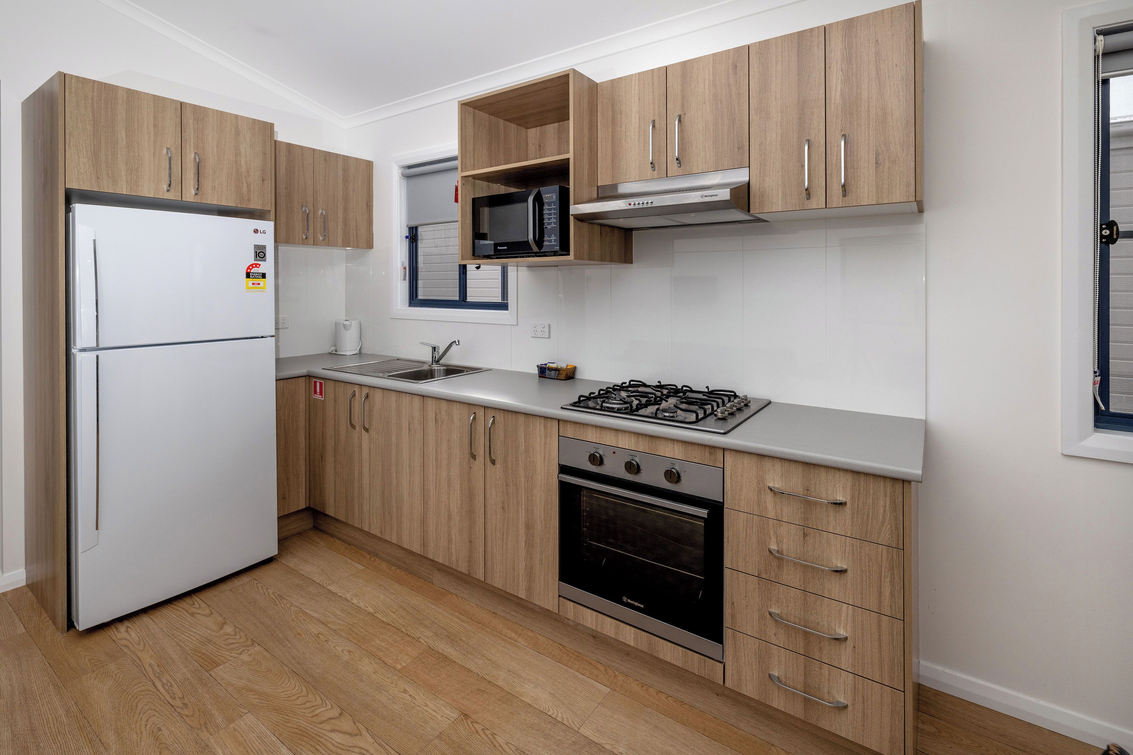 Een moderne keuken met houten kastjes, een witte koelkast, een magnetron, een gasfornuis en een oven.