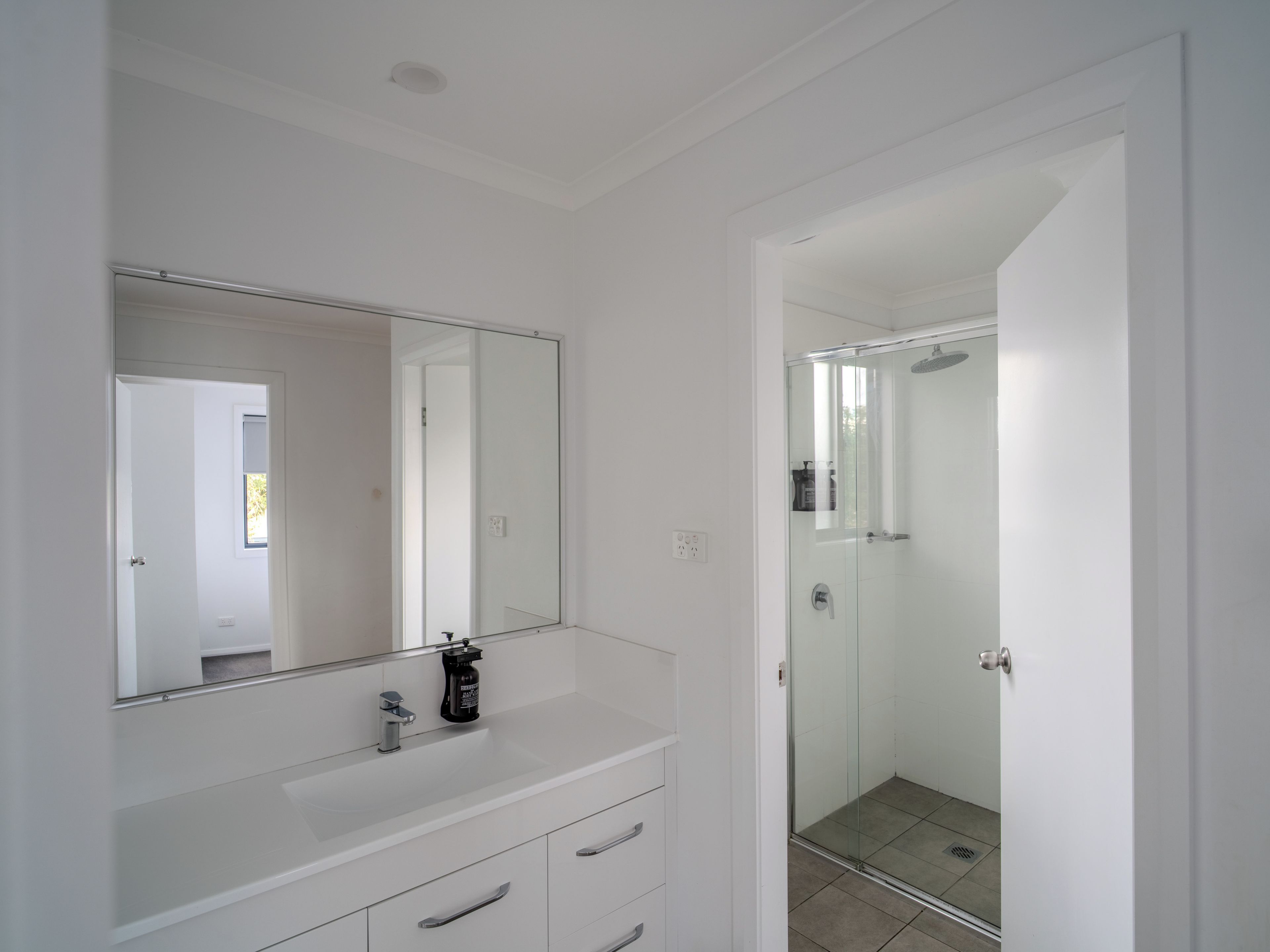 Un baño moderno con tocador blanco, un espejo grande y cabina de ducha con paredes de vidrio.