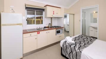 A compact hotel room with a kitchenette, a bed with a patterned bedspread, and a bathroom with a mirror and sink.